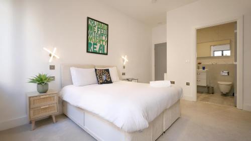 a bedroom with a large white bed and a bathroom at Stunning Acton Apartment With Patio in London