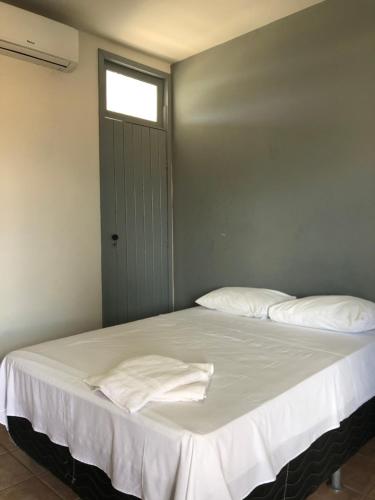 a bedroom with a bed with white sheets and a window at Pousada Praia Do Farol in Alcobaça