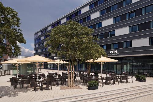 een cafetaria met tafels en parasols voor een gebouw bij INNSiDE by Meliá Wolfsburg in Wolfsburg