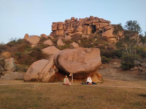 two people sitting on the ground in front of a rock at Hill Stone View Hampi in Hampi