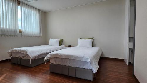 Habitación con 2 camas, paredes blancas y suelo de madera. en Parkcliffe, en Jeju