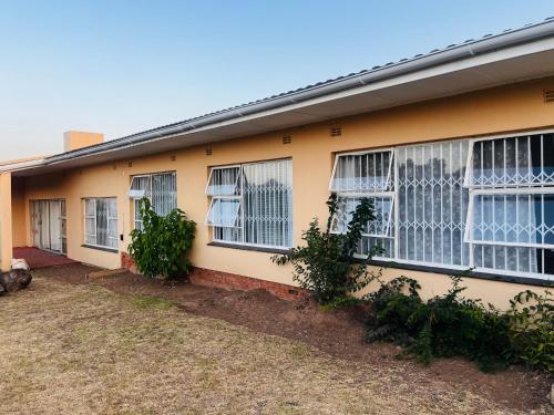 a yellow house with white windows and bushes at Lavender Lodge Twin in Mthatha