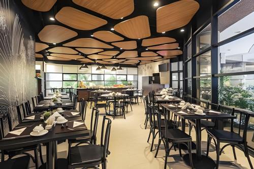 un restaurante con mesas negras, sillas y ventanas en Get a Flat 1403 localização Nobre en São Paulo