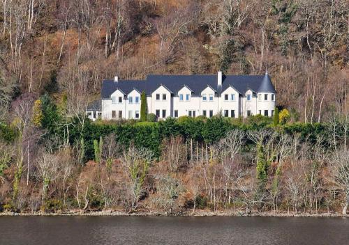 a large white house on a hill next to the water at Loch Ness Lodge in Drumnadrochit