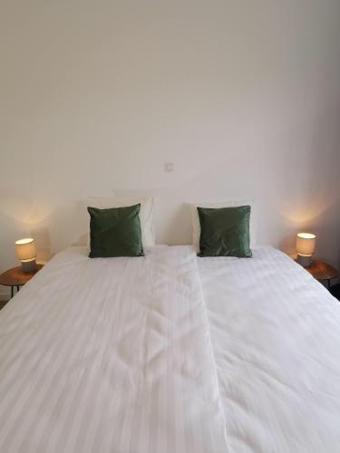 a white bed with two green pillows on it at Ten Velde - vakantiewoning 12 personen - sauna - bubbelbad in Hoeselt