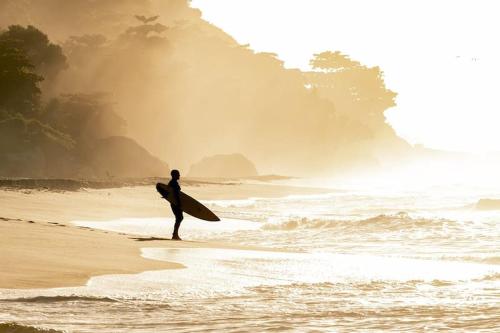 Un uomo in piedi sulla spiaggia con una tavola da surf di Suítes Luxo Marambaia- Epic House a Rio de Janeiro