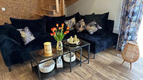 eine schwarze Couch mit Kissen und einen Tisch mit Blumen in der Unterkunft Domki Lubiane in Brenna