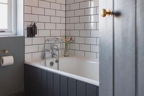 La salle de bains est pourvue d'une baignoire et de carrelage blanc. dans l'établissement Park Cottage, à Sedgeford