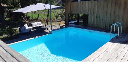 - une piscine avec un parasol à côté d'une maison dans l'établissement la paisible Landaise, à Sainte-Eulalie-en-Born