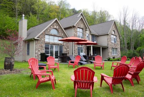 a group of red chairs and umbrellas in front of a house at Grand Slam Lake House Cooperstown Dreams Park in Cooperstown