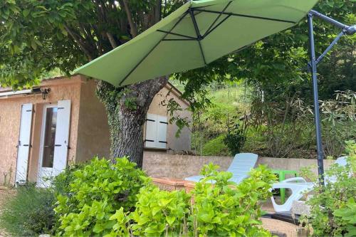 a green umbrella and two chairs and a tree at Mini villa de charme. in Zonza