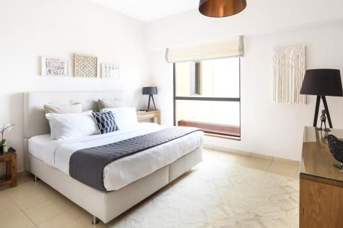 a white bedroom with a bed and a window at Frank Porter - Sadaf 6 in Dubai