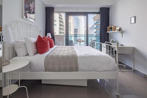 a white bedroom with a large bed with red pillows at Frank Porter - Merano Tower in Dubai