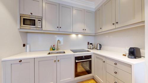 a white kitchen with white cabinets and a microwave at The Wimpole IX - 1 bed flat in London