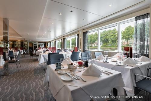 um restaurante com mesas e cadeiras brancas e janelas em KD Hotelship Frankfurt Untermainkai em Frankfurt am Main
