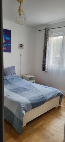 a bedroom with a bed with a blue comforter and a window at Paris/La Défense 10' en train 2 CHB in Colombes