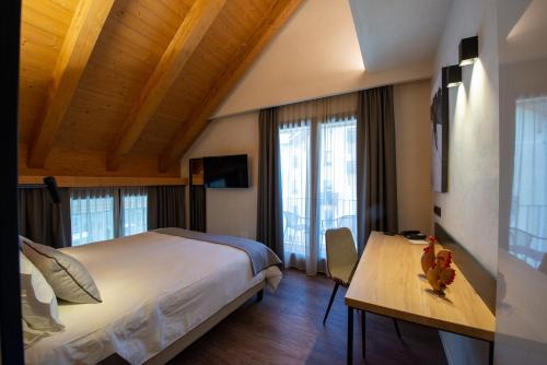 Schlafzimmer mit einem großen Bett, einem Schreibtisch und Fenstern in der Unterkunft Hotel Sant'Orso - Mountain Lodge & Spa in Cogne