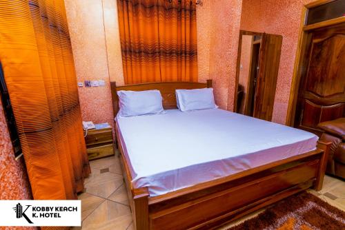 Una cama con sábanas blancas en una habitación pequeña. en Kobby Keach K. Hotel, en Kumasi