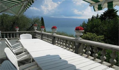 a table and chairs on a balcony with a view of the ocean at Villa Pinetina in Gargnano