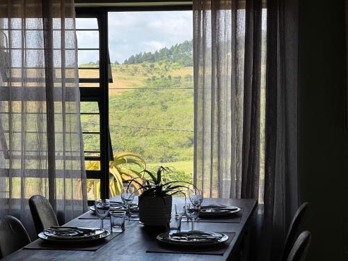 a table with plates and wine glasses in front of a window at ALOE cottage Valley of a 1000 hills in Drummond