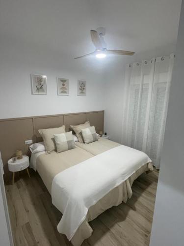 a white bedroom with a large bed and a ceiling fan at Apartamento Vitelio in Carmona