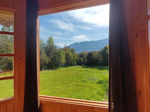 a window with a view of a green field at Cabaña Queltehue Cochamó in Cochamó