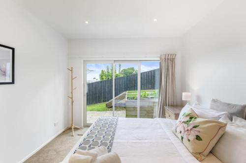 Dormitorio blanco con cama y puerta corredera de cristal en Sensational Rest in the North, en Auckland