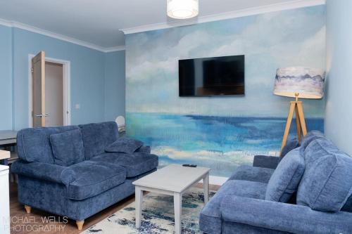 a living room with two blue couches and a painting at Capstone's Lookout near tunnels beach in Ilfracombe