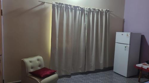 a room with a white curtain and a chair and a refrigerator at Hostal Ña Lali in Villarrica