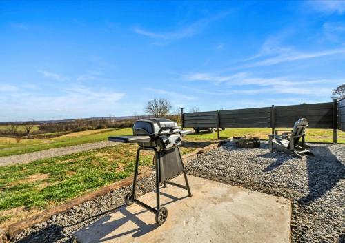a grill on a stand in front of a bench at Cozy 2-Guest RV on Nature Farm in Pine Grove