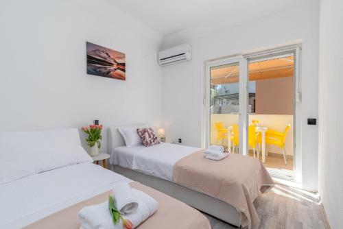 a white bedroom with two beds and a balcony at Aldino Rooms in Trogir