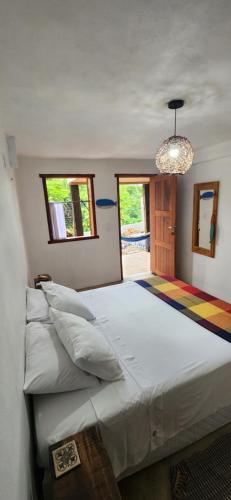 um quarto com uma grande cama branca e um lustre em Suítes da Quinta dos Samaniegos em Itaúnas