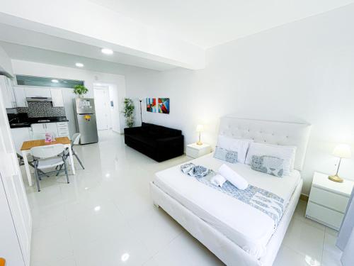 a white bedroom with a large bed and a kitchen at DUCASSI SUITE Sol Karibe SUITES STUDIOS TROPICANA Rooftop POOL WiFi Beach & SPA in Punta Cana