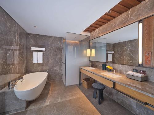 baño con bañera grande y espejo grande en DoubleTree by Hilton Changbaishan Hot Spring, en Antu