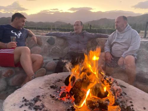 a group of three men sitting around a fire at Ruedas Negras Casa de Campo in Los Árboles