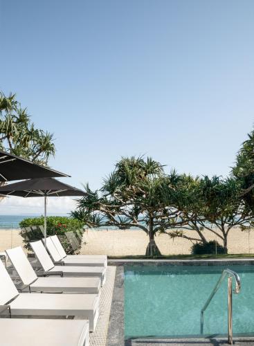 a pool with chairs and an umbrella and the beach at Netanya Noosa Beachfront Resort in Noosa Heads