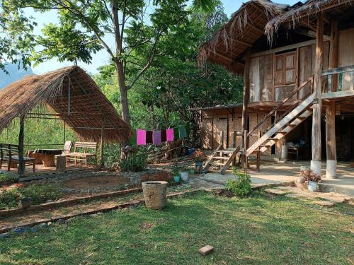 una casa con techo de paja y algunas sillas y árboles en Mường Trai Homestay, en Sơn La