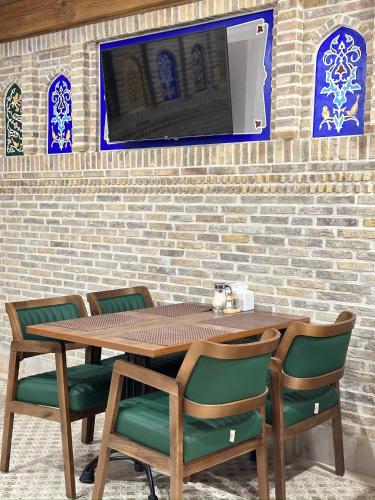 a wooden table with chairs and a tv on a brick wall at Istat Boutique Hotel in Bukhara