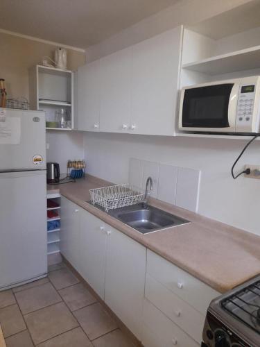 una cucina bianca con lavandino e forno a microonde di Departamento en el Tabo a El Tabo