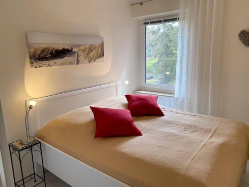 um quarto com uma cama com duas almofadas vermelhas em Haus-Utlande-Whg-34 em Sankt Peter-Ording
