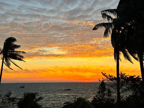 a sunset on the beach with palm trees and the ocean at Khalid’s House at the East coast in Phu Quoc
