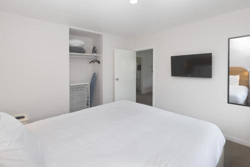 a white bedroom with a bed and a tv at The Adelphi in Christchurch