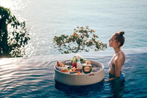 a woman standing in the water with a basket of food at Cape Fahn Hotel Samui in Choeng Mon Beach