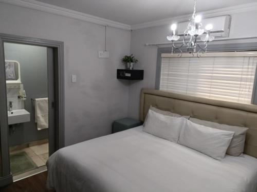 - une chambre avec un lit blanc et un lustre dans l'établissement Camdene Guesthouse, au Cap