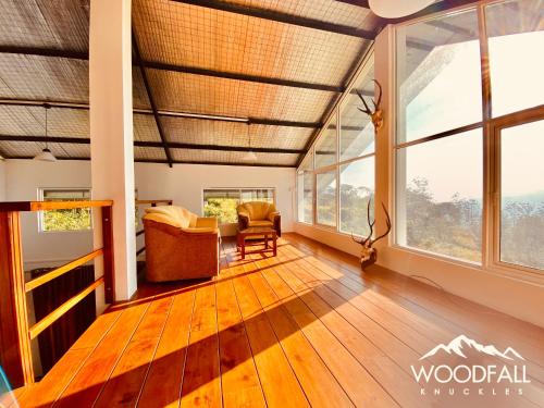 een woonkamer met houten vloeren en grote ramen bij Woodfall Knuckles - Holiday Bungalow in Panwila