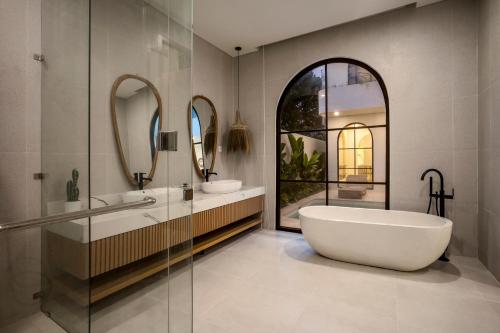 uma casa de banho com banheira, 2 lavatórios e espelhos em Villa Balmoral Canggu em Canggu