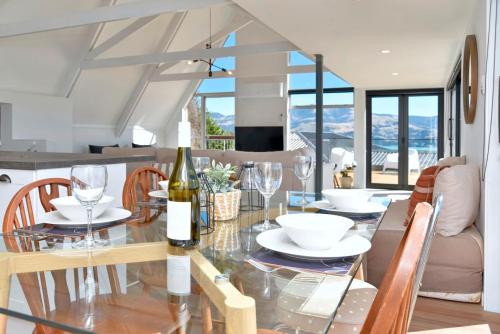 Akaroa Harbour View - Christchurch Holiday Homes في أكارو: غرفة طعام مع طاولة زجاجية مع كؤوس للنبيذ