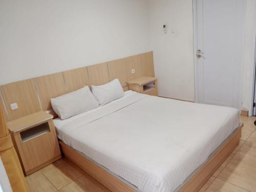 Schlafzimmer mit einem weißen Bett mit einem Kopfteil aus Holz in der Unterkunft Macan Kumbang Residence in Palembang