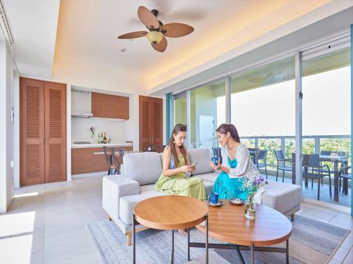 two women sitting on a couch in a living room with a laptop at The Pool & Sauna Villa MOTOBU in Motobu