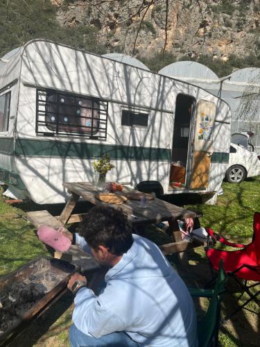 un homme assis sur une table de pique-nique devant une remorque dans l'établissement Caravan camp, à Erdemli